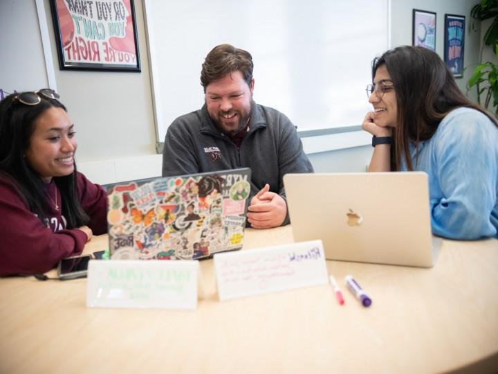 Director of Student Success sits with students at a table during a tutoring session